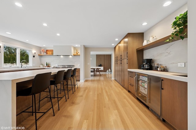 kitchen with open shelves, light countertops, light wood-style floors, a kitchen bar, and backsplash