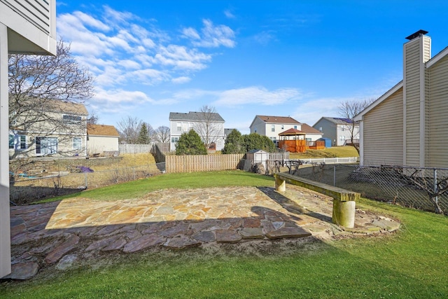 view of yard featuring a residential view, a fenced backyard, an outbuilding, a storage unit, and a patio