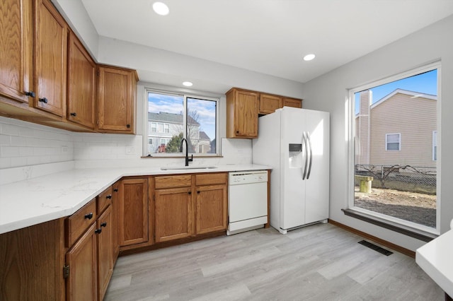 kitchen with brown cabinetry, visible vents, white appliances, and a sink