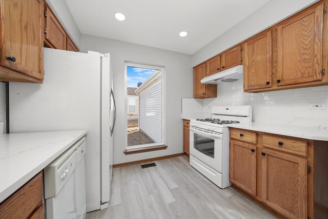 kitchen with visible vents, brown cabinets, under cabinet range hood, tasteful backsplash, and white appliances