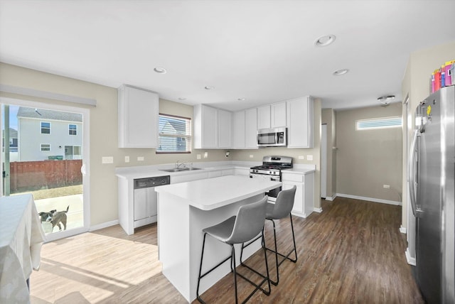 kitchen with dark wood finished floors, a sink, stainless steel appliances, light countertops, and a kitchen breakfast bar