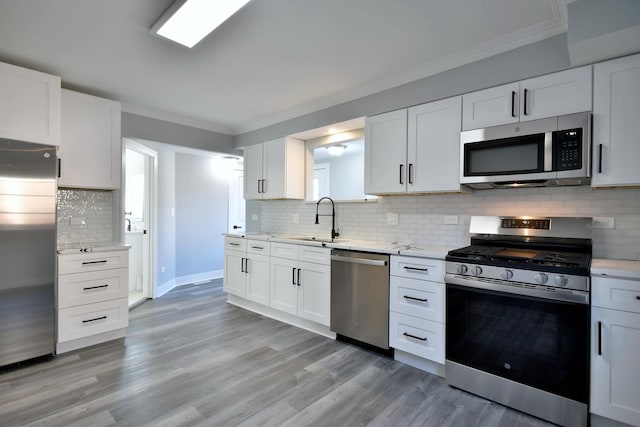 kitchen featuring white cabinets, stainless steel appliances, crown molding, and a sink