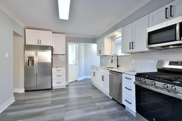 kitchen with light stone counters, ornamental molding, a sink, white cabinets, and appliances with stainless steel finishes