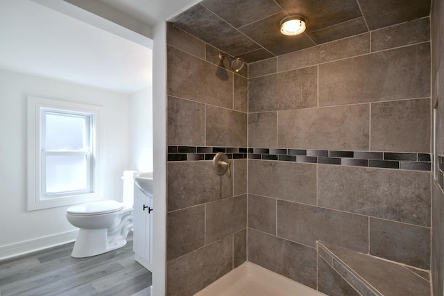 full bathroom with a tile shower, toilet, vanity, and wood finished floors