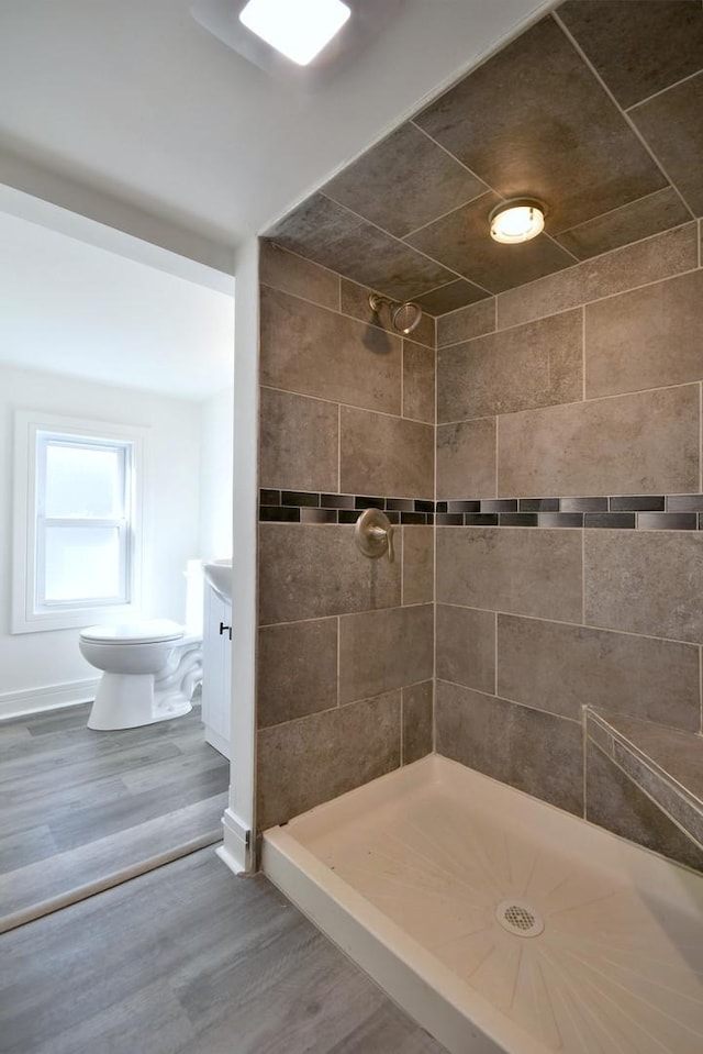 bathroom featuring toilet, wood finished floors, baseboards, and tiled shower