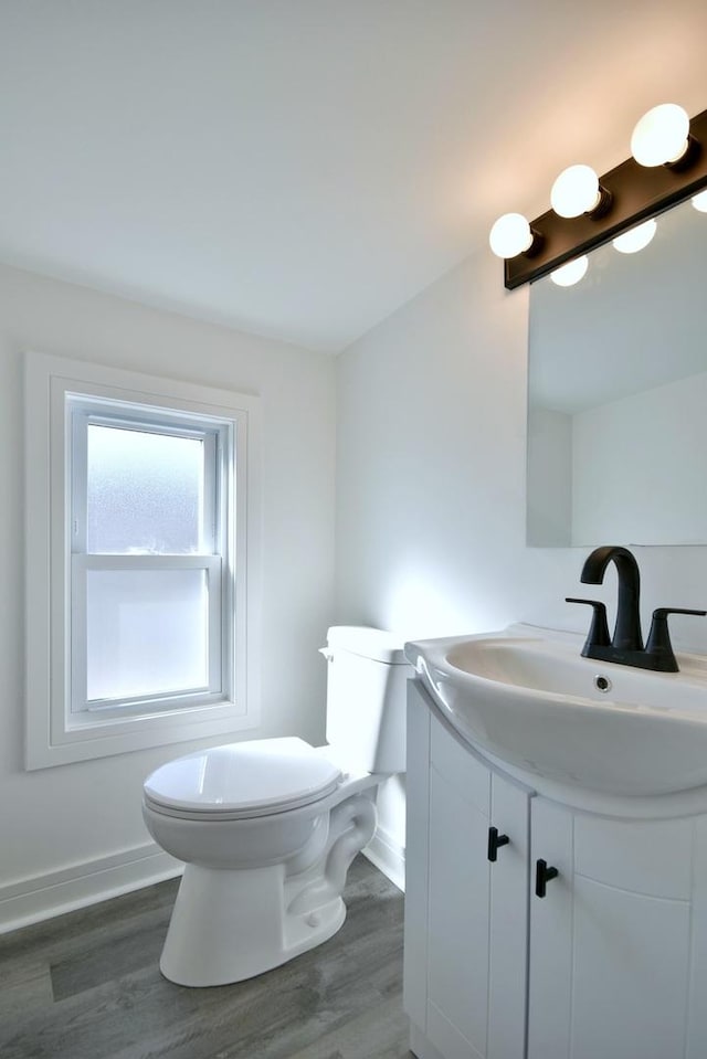 half bathroom with toilet, vanity, baseboards, and wood finished floors