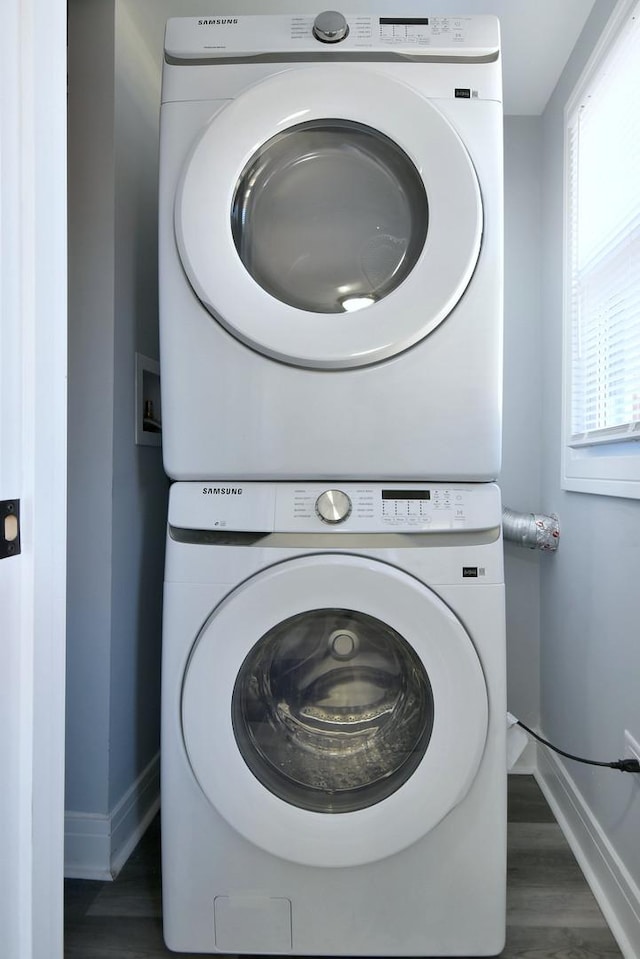 laundry room featuring baseboards, wood finished floors, laundry area, and stacked washer / dryer