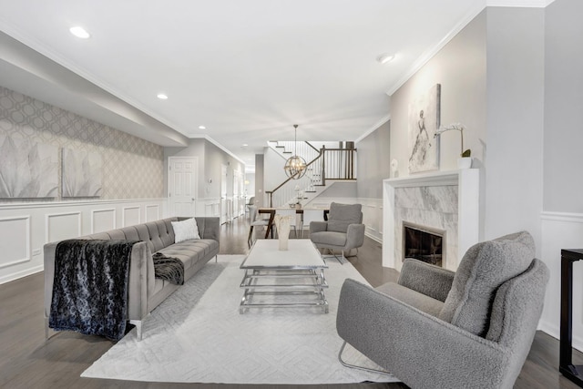 living room with a tiled fireplace, a wainscoted wall, stairs, and wood finished floors