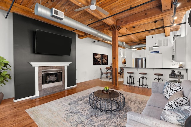 living area featuring visible vents, a tiled fireplace, wood ceiling, wood finished floors, and a ceiling fan