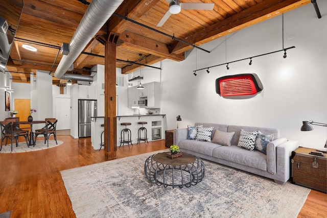 living area with beamed ceiling, wood finished floors, a towering ceiling, wooden ceiling, and ceiling fan