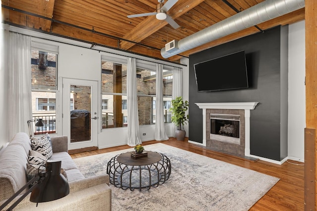 living room featuring wood finished floors, beam ceiling, ceiling fan, a tile fireplace, and wood ceiling