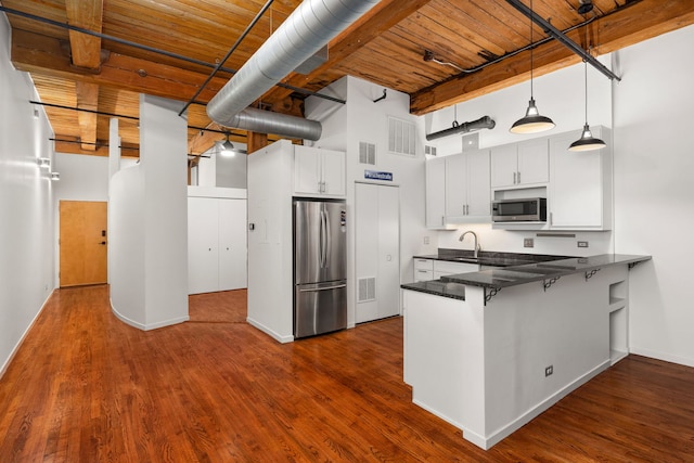 kitchen featuring a breakfast bar area, a peninsula, a towering ceiling, stainless steel appliances, and dark wood-style flooring