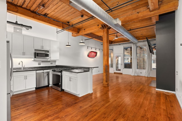 kitchen featuring a peninsula, a sink, stainless steel appliances, dark countertops, and wooden ceiling