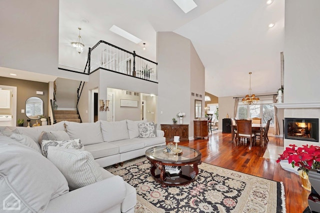 living room with stairway, wood finished floors, a skylight, a glass covered fireplace, and a chandelier