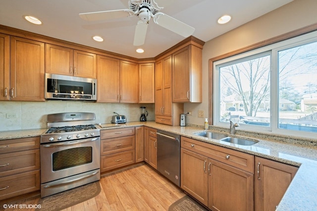 kitchen featuring light stone countertops, light wood-style flooring, brown cabinetry, stainless steel appliances, and a sink