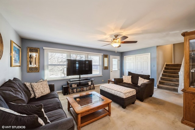 living area with baseboards, light colored carpet, ceiling fan, and stairs