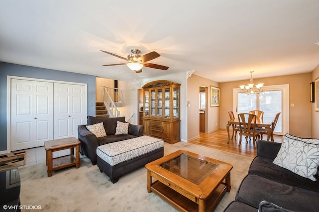 living area featuring stairway, baseboards, and ceiling fan with notable chandelier