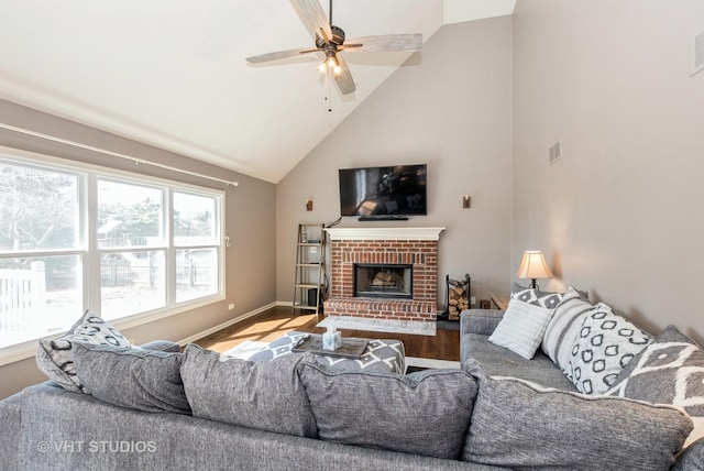 living room with baseboards, ceiling fan, a fireplace, wood finished floors, and high vaulted ceiling