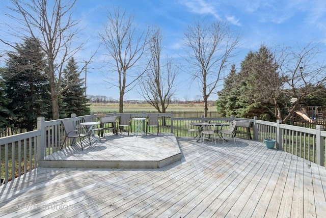 deck featuring outdoor dining space, a rural view, a playground, and fence