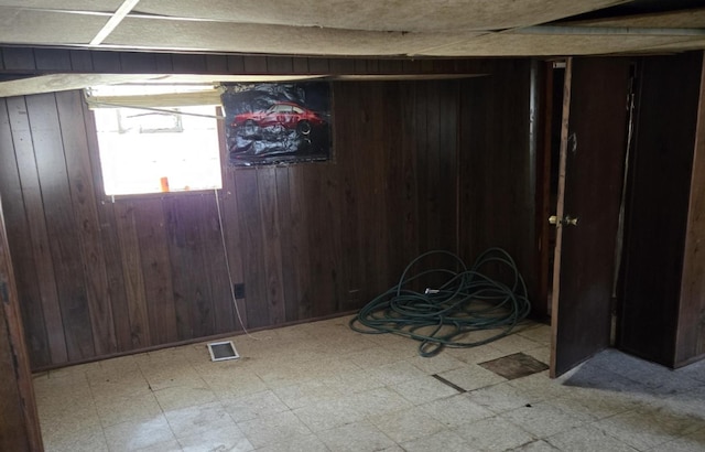 basement featuring tile patterned floors, wooden walls, and visible vents