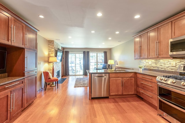 kitchen featuring a peninsula, light wood-type flooring, appliances with stainless steel finishes, and a sink