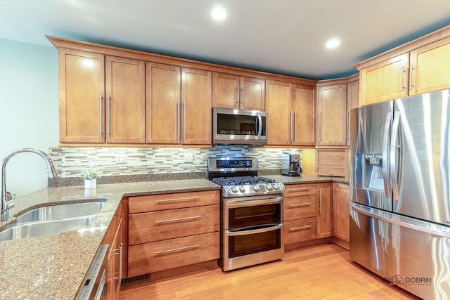 kitchen with a sink, light wood-style floors, tasteful backsplash, and stainless steel appliances