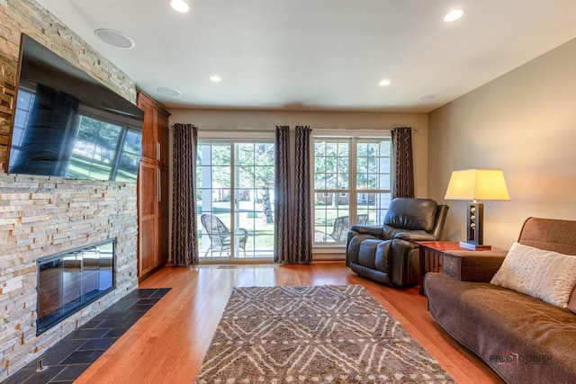 living room with a stone fireplace, recessed lighting, and wood finished floors