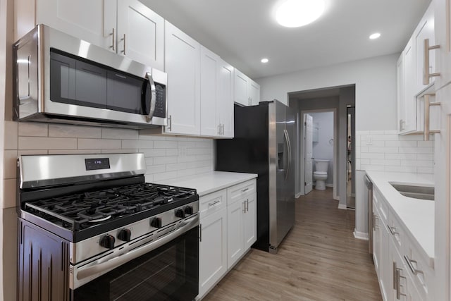 kitchen with backsplash, white cabinetry, stainless steel appliances, light wood-style floors, and light countertops