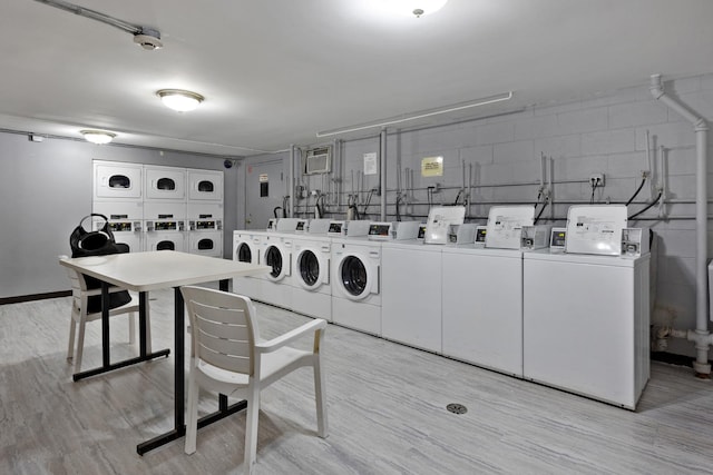 common laundry area featuring concrete block wall, light wood-style floors, stacked washer and clothes dryer, and washing machine and clothes dryer