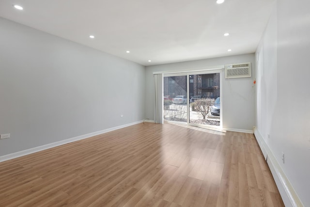 spare room featuring light wood finished floors, recessed lighting, a wall mounted AC, and baseboards