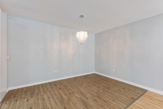 empty room featuring wood finished floors, baseboards, and a chandelier