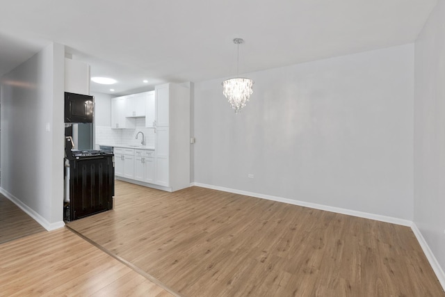 interior space with a sink, black appliances, white cabinets, light wood-type flooring, and backsplash