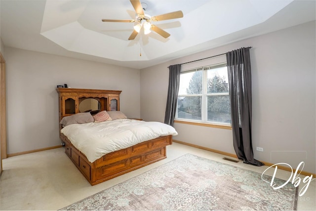 bedroom featuring visible vents, light carpet, baseboards, a tray ceiling, and a ceiling fan