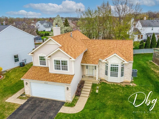 view of front of property with a shingled roof, a garage, a front yard, central air condition unit, and driveway