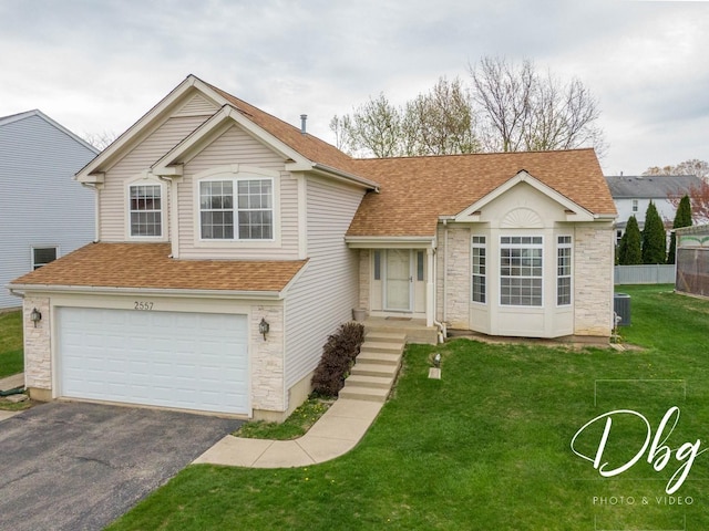 split level home with driveway, a front yard, a garage, a shingled roof, and stone siding