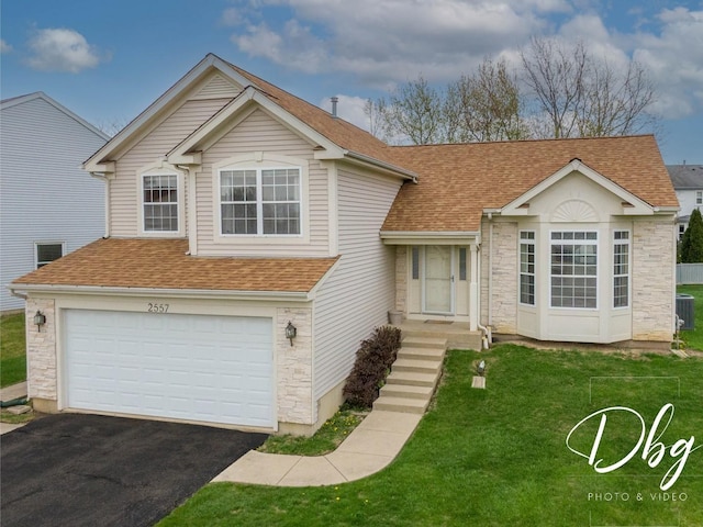 split level home with driveway, a front yard, roof with shingles, an attached garage, and stone siding
