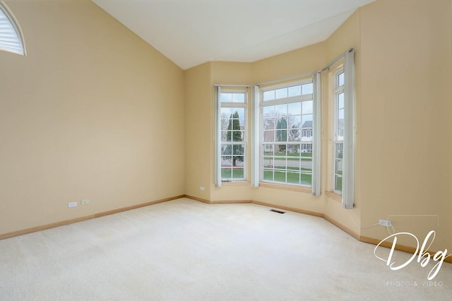 carpeted spare room with baseboards, visible vents, and lofted ceiling
