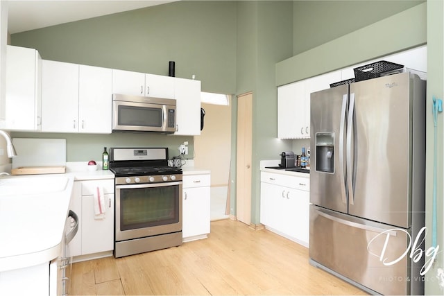 kitchen featuring high vaulted ceiling, light wood-type flooring, white cabinets, a sink, and appliances with stainless steel finishes