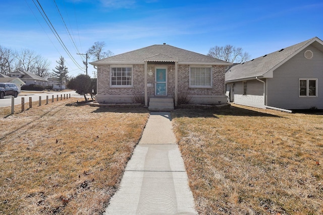 bungalow-style home with brick siding, a shingled roof, and a front lawn