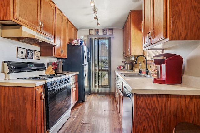 kitchen featuring light wood finished floors, under cabinet range hood, gas range, dishwasher, and a sink