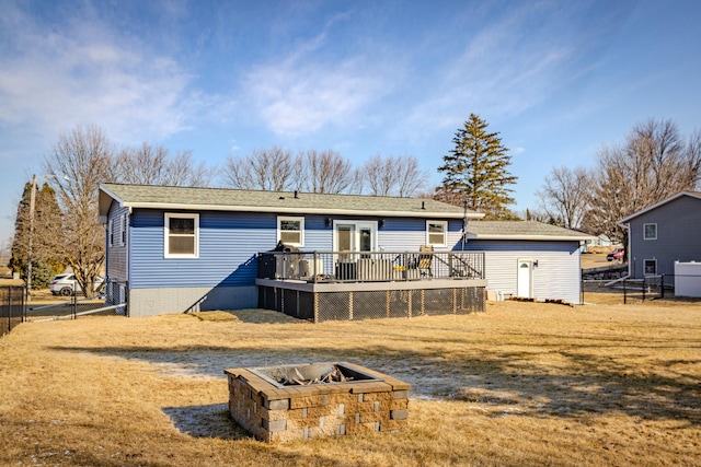 rear view of property featuring a wooden deck, a lawn, an outdoor fire pit, and fence