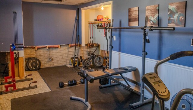 exercise room with a paneled ceiling and wainscoting