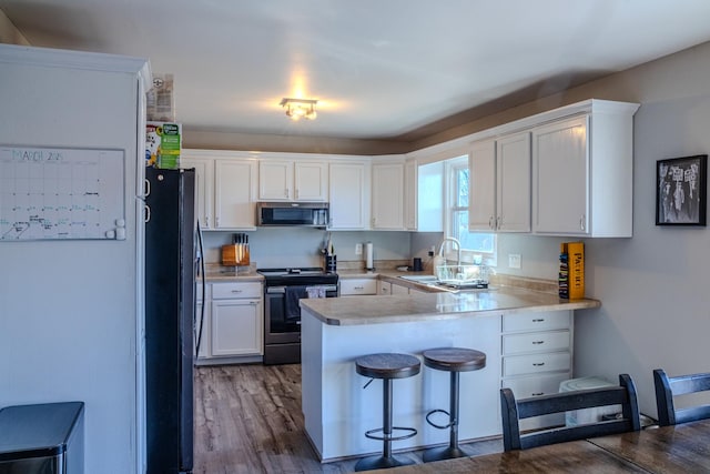 kitchen featuring a kitchen bar, appliances with stainless steel finishes, a peninsula, white cabinetry, and a sink