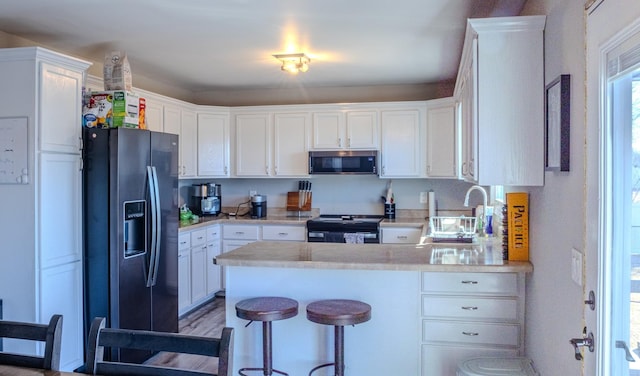 kitchen with white cabinets, a peninsula, stainless steel appliances, and a sink