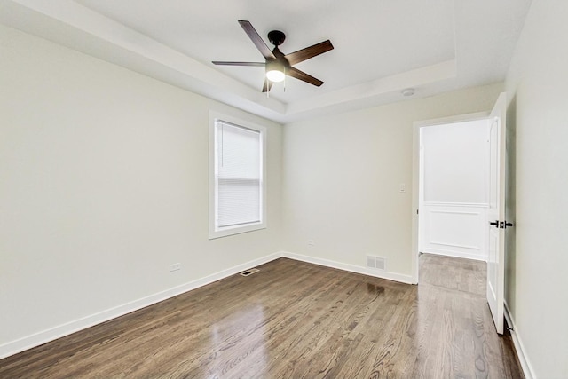 spare room featuring a ceiling fan, baseboards, visible vents, dark wood-type flooring, and a raised ceiling