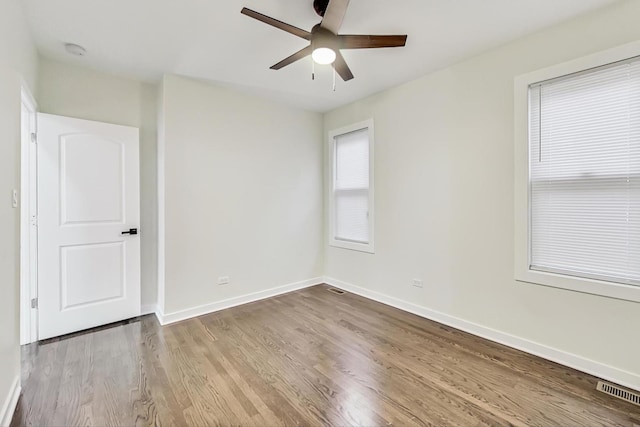 empty room with ceiling fan, visible vents, baseboards, and wood finished floors