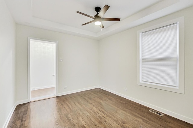 empty room featuring visible vents, dark wood-type flooring, a ceiling fan, baseboards, and a raised ceiling