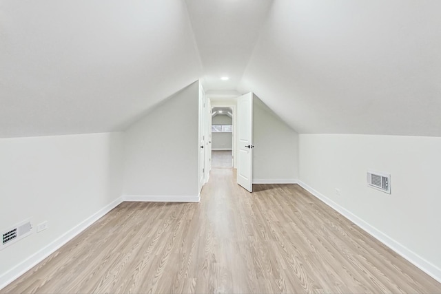 additional living space featuring visible vents, light wood-type flooring, baseboards, and vaulted ceiling