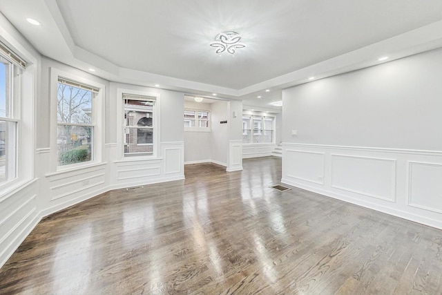 empty room with a wealth of natural light, visible vents, wood finished floors, and a decorative wall