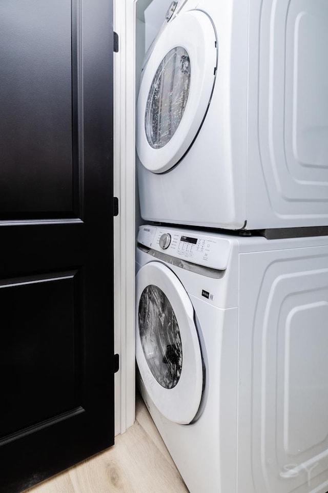 clothes washing area with light wood finished floors, laundry area, and stacked washer and dryer